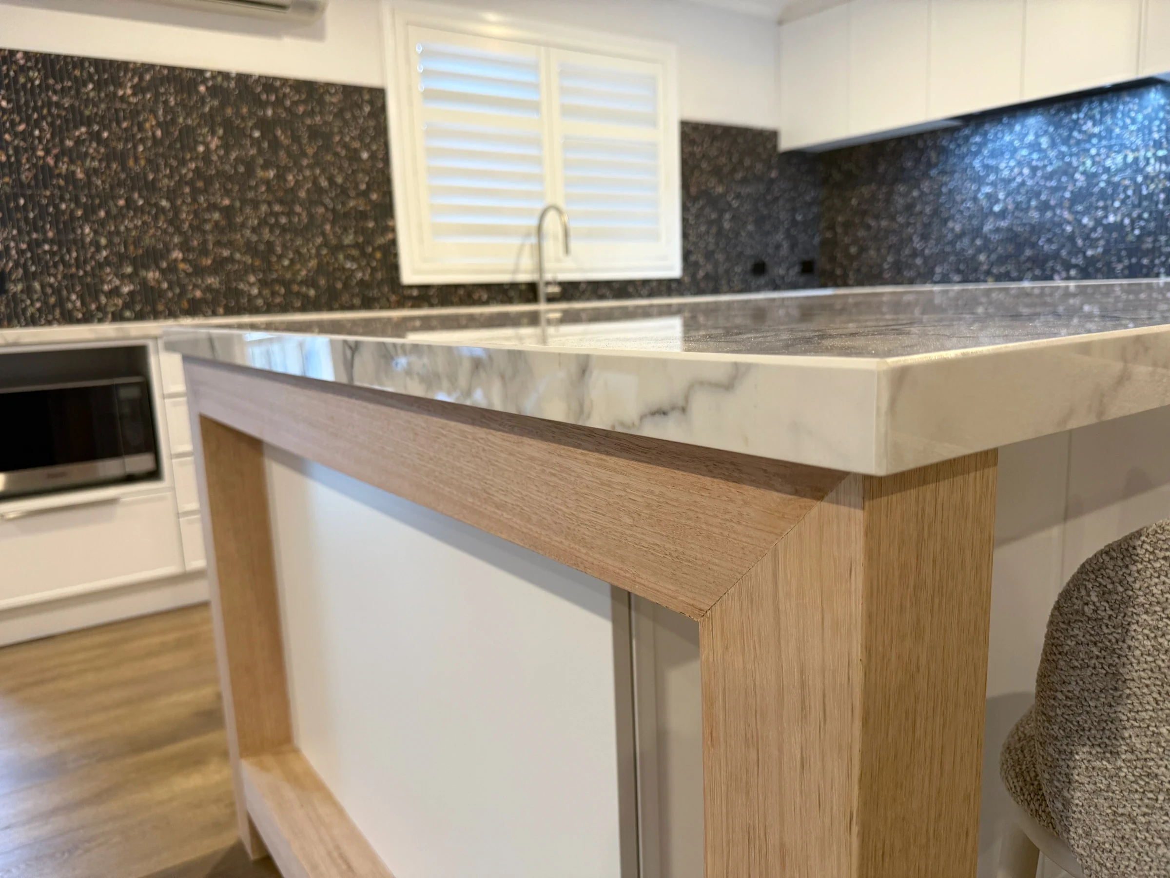 Stone benchtop edge resting above the timber island frame in the completed Bluestone kitchen
