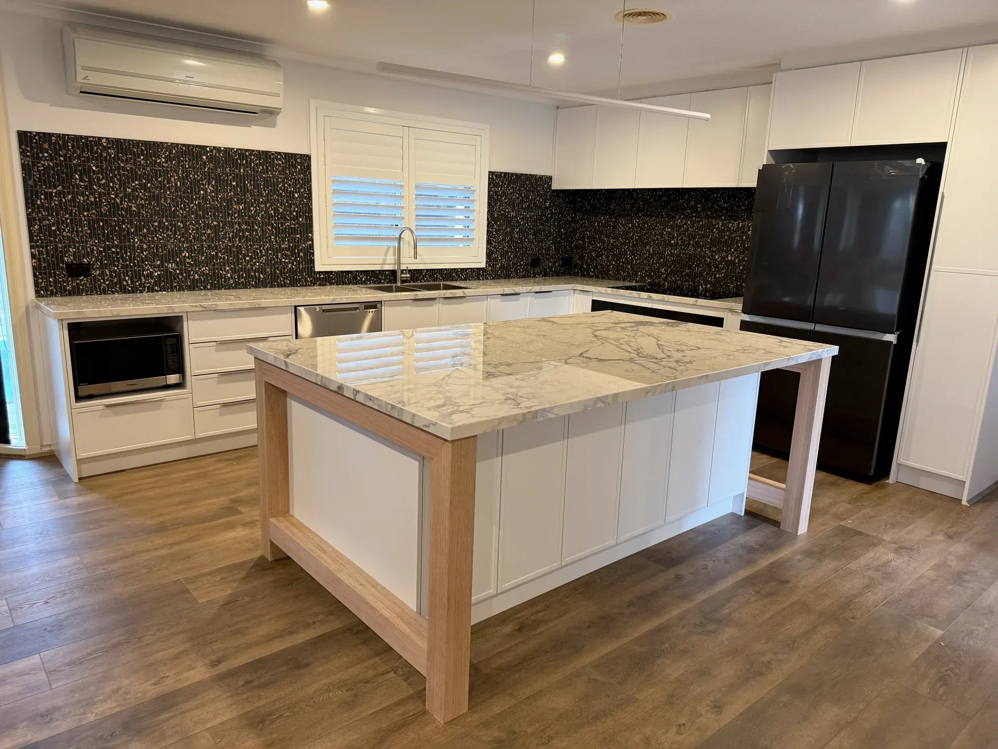 Completed Bluestone kitchen in Point Cook with white cabinetry, timber-framed island and dark tiled splashback